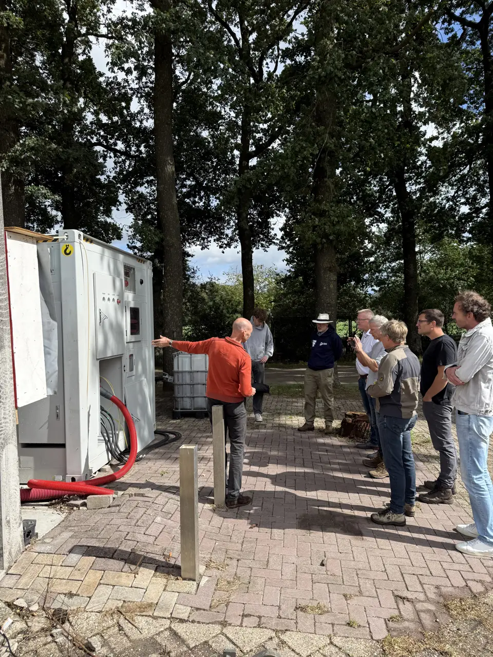 Bezoekers staan op de bestrating naast de witte container van de Vrije Netaansluiting en luisteren naar de uitleg